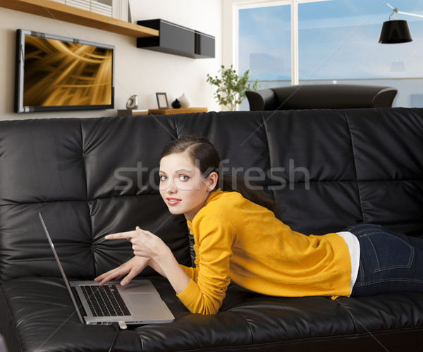 girl on sofa with laptop, she indicates the display with one fin Stock photo © carlodapino