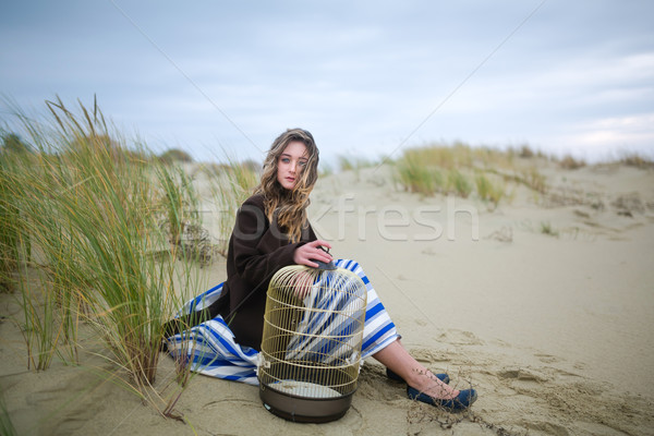 Stock photo: Beautiful girl with a birdcage in a dune