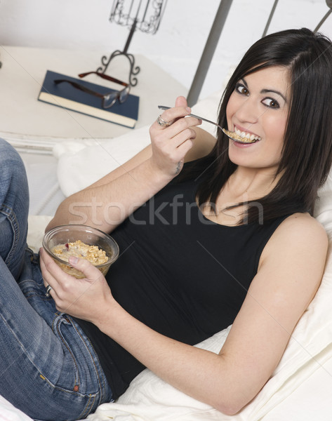 Smiling Young Adult Woman Eats Cereal With Fruit on Bed Stock photo © cboswell
