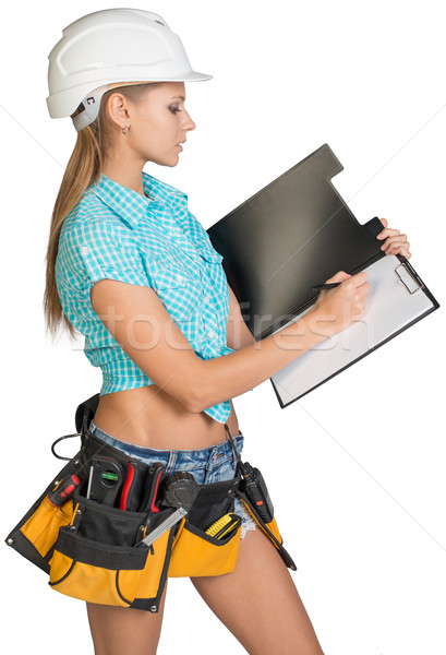 Woman in hard hat and tool belt writing on blank clipboard Stock photo © cherezoff
