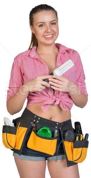 Stock photo: Woman in tool belt holding energy-saving lamp