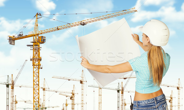 Woman in helmet standing backwards and holding paper sheet. Tower cranes as backdrop Stock photo © cherezoff