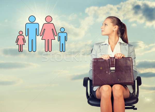 Stock photo: Business woman in skirt, blouse and jacket, sitting on chair, holding briefcase imagines family. Aga
