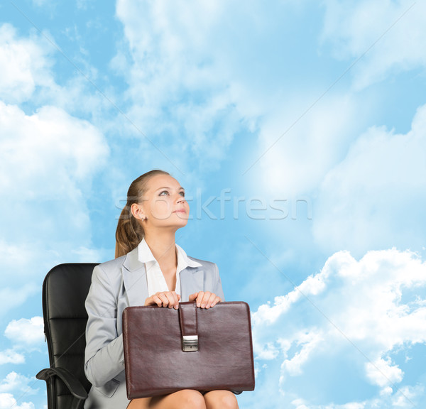 Business woman in skirt, blouse and jacket, sitting on chair, holding briefcase. Against background  Stock photo © cherezoff