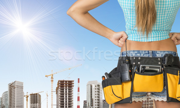 Woman in tool belt stands back. Hands on hip. Building and sky as backdrop Stock photo © cherezoff