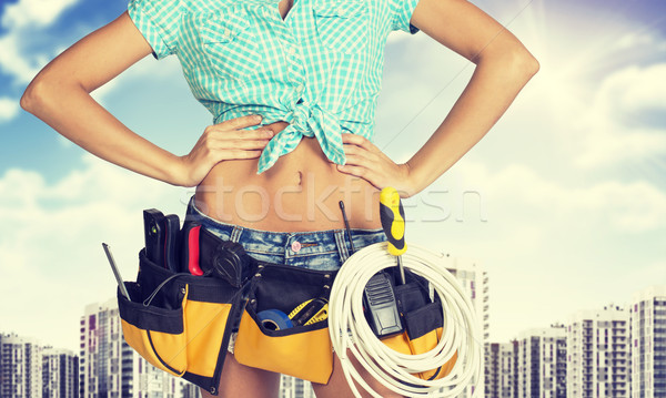 Woman in tool belt standing akimbo. Cropped image. High-rise buildings as backdrop Stock photo © cherezoff