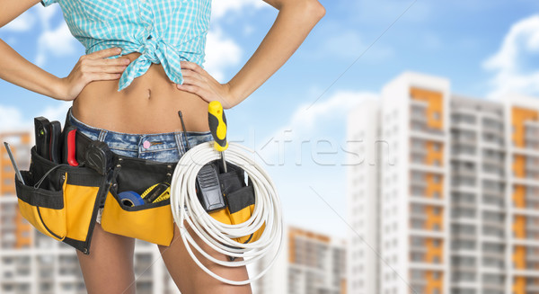 Woman in tool belt. Hands on hip. Buildings and sky as backdrop Stock photo © cherezoff