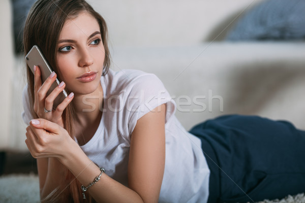 Young woman calling by her smart phone lying on floor Stock photo © chesterf