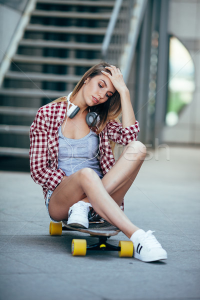 young adult woman sitting on longboard and wearing headphones Stock photo © chesterf