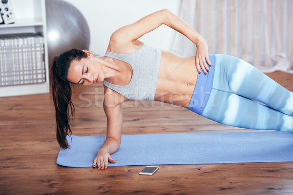 Slim fitness young woman doing side plank exercise at home with smartphone Stock photo © chesterf