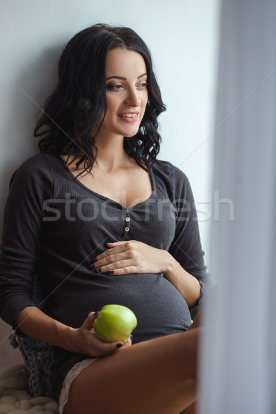 Cute happy pregnant woman on window sill with apples in the room, close up Stock photo © chesterf