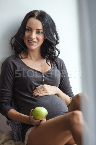 Cute happy pregnant woman on window sill with apples in the room, close up Stock photo © chesterf