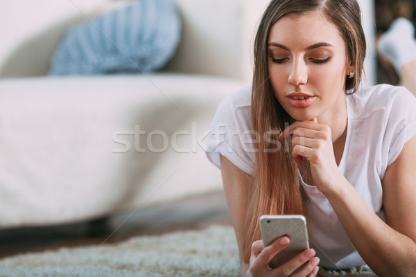 Young woman checking her smart phone lying on carpet Stock photo © chesterf
