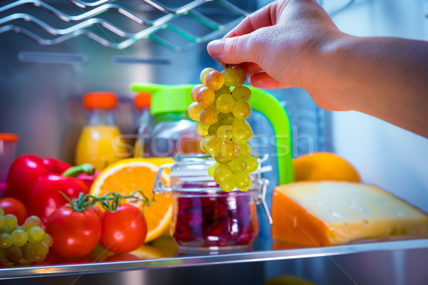 Woman takes the bunch of grapes from the open refrigerator Stock photo © cookelma