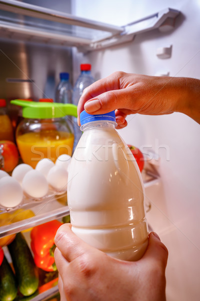 Stock photo: Woman takes the milk from the open refrigerator