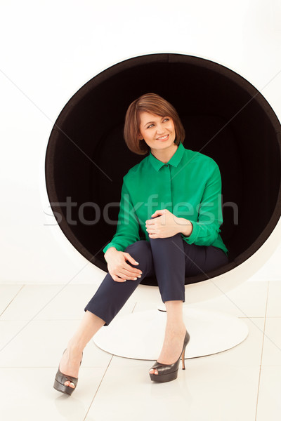 Red haired smiling woman looking away while sitting on modern chair Stock photo © d13