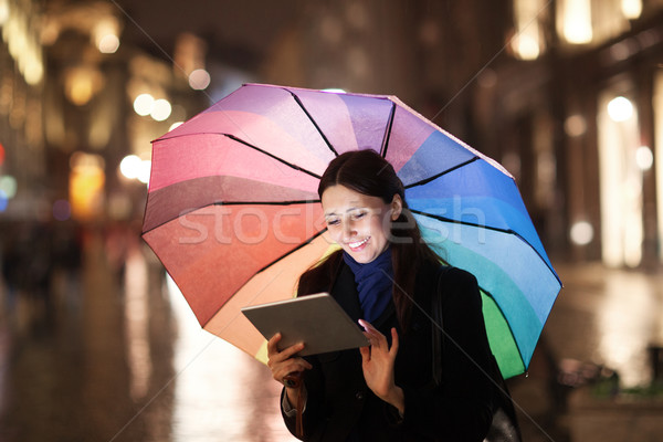 Woman using pad under umbrella in the evening city Stock photo © d13