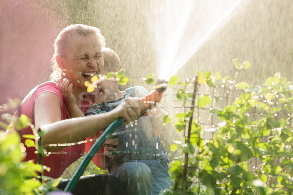 Laughing mother and son playing with a sprinkler Stock photo © d13
