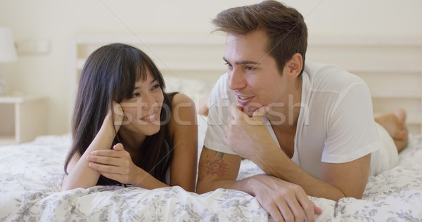 Smiling couple talking while laying down on bed Stock photo © dash
