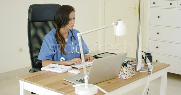 Stock photo: Young female doctor sitting typing in her office