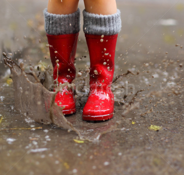 Child wearing red rain boots jumping into a puddle Stock photo © dashapetrenko