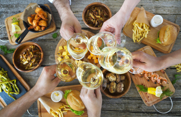 Stock photo: People with white wine toasting over served table with food.