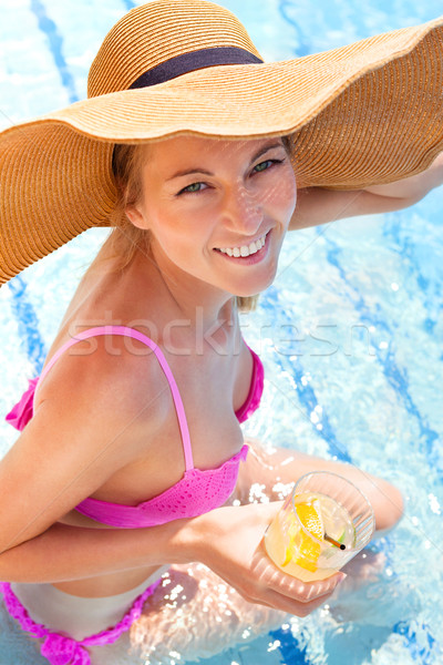 Stock photo: Woman in a hat enjoying cocktail in a swimming pool