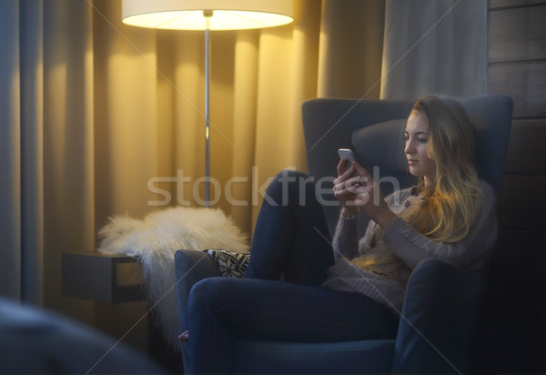 Woman lying on armchair while writing a text message on her cell Stock photo © dashapetrenko