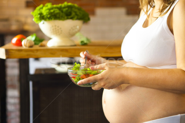 Young pregnant woman eating fresh vegetable salad at the kitchen Stock photo © dashapetrenko