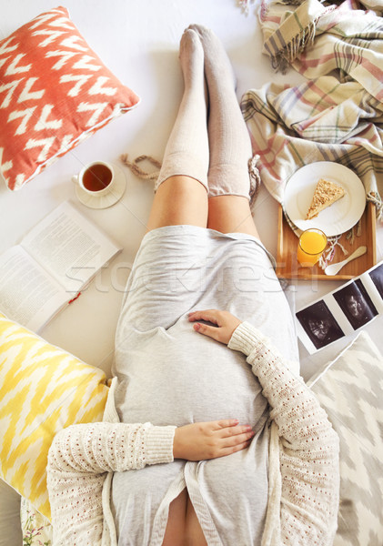 Stock photo: Pregnant woman with book, tea, cake relaxing at home