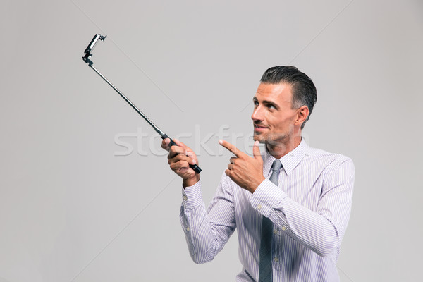 Handsome businessman holding selfie stick Stock photo © deandrobot
