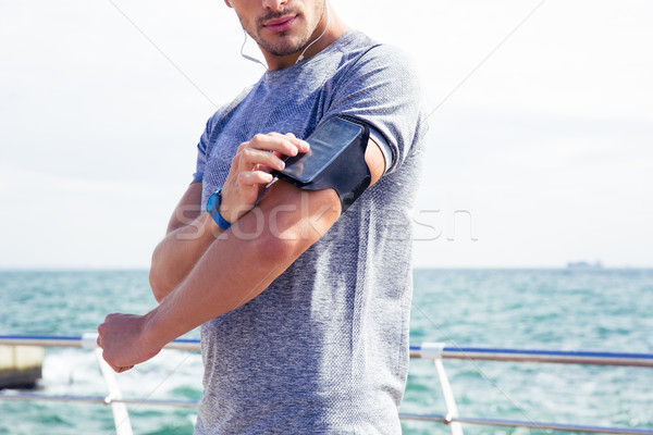 Stock photo: Male runner listening to music adjusting settings on armband for smartphone