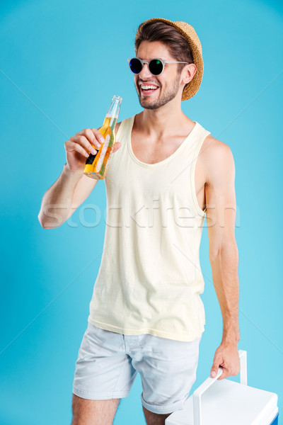 Cheerful young man holding cooler bag and drinking beer Stock photo © deandrobot