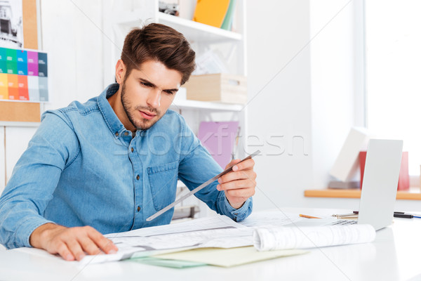 Young man architect holding ruler over diagram on the desk Stock photo © deandrobot