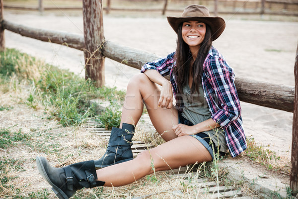 Smiling happy cowgirl sitting and resting at the ranch fence Stock photo © deandrobot