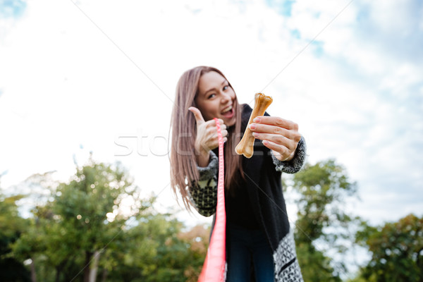 Cheerful woman giving bone to dog and showing thumbs up Stock photo © deandrobot