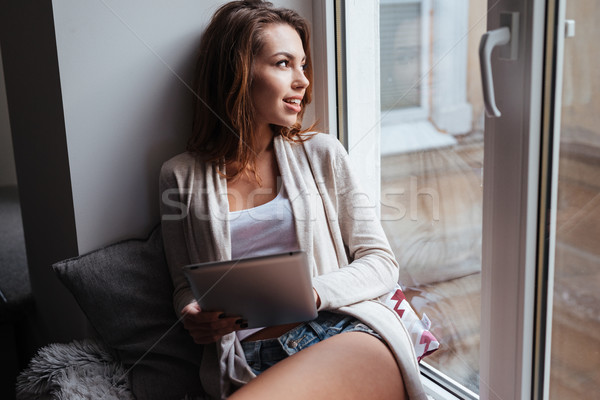 Woman sitting on windowsill with tablet computer Stock photo © deandrobot