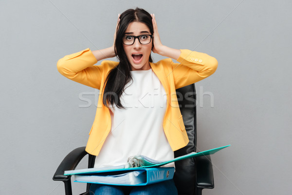 Confused woman holding folders while sitting and looking at camera Stock photo © deandrobot