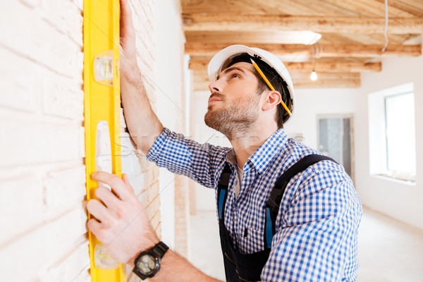 Builder in uniform holding a level against the wall indoors Stock photo © deandrobot