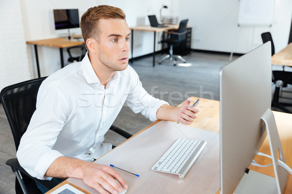 Pensive young businessman sitting and working with computer Stock photo © deandrobot