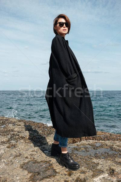 Woman in sunglasses and black coat walking on seashore Stock photo © deandrobot