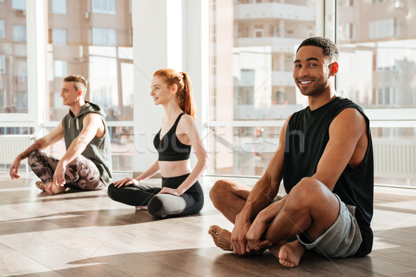 Happy african young man sitting and doing yoga in group Stock photo © deandrobot