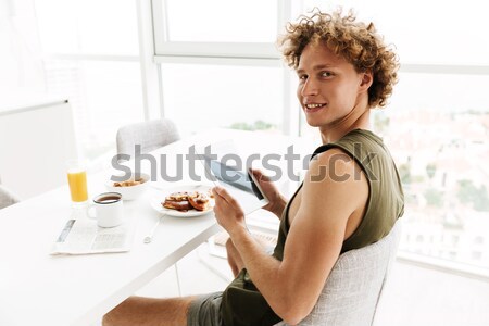 Pleased casual woman eating by the table on kitchen Stock photo © deandrobot