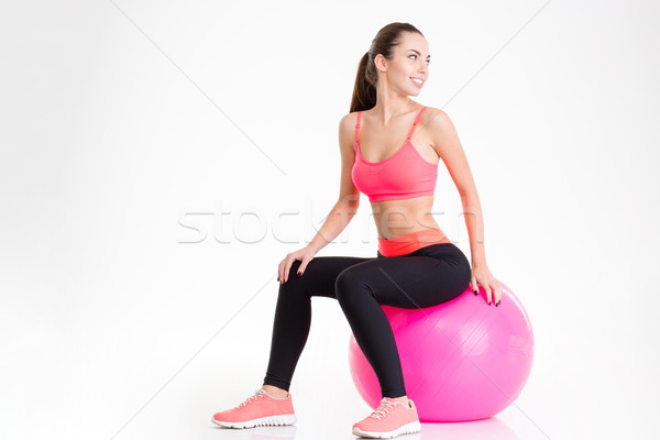 Cheerful pretty young fitness woman sitting on pink fitball  Stock photo © deandrobot