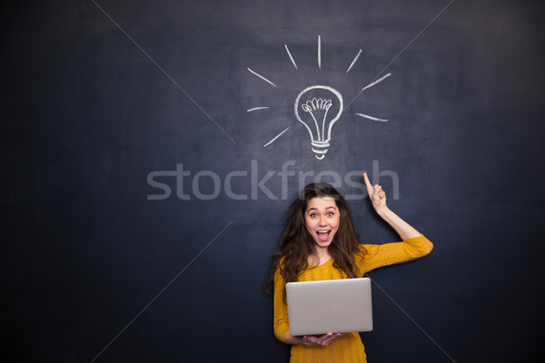 Happy woman holding laptop and having idea over blackboard background Stock photo © deandrobot