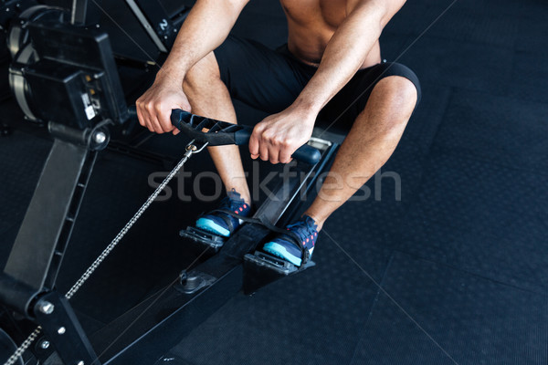 Stock photo: Muscular fitness man using rowing machine in the gym
