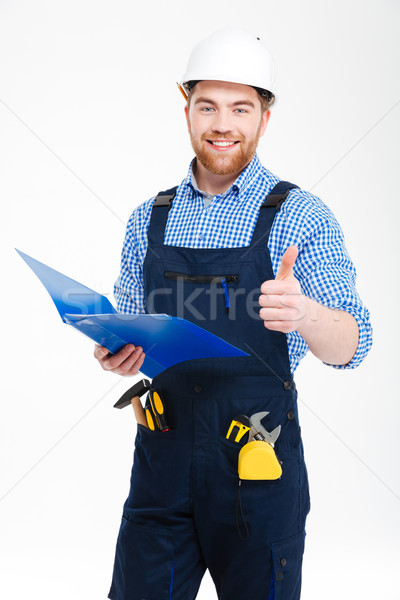 Smiling successful young builder using clipboad and showing thumbs up Stock photo © deandrobot