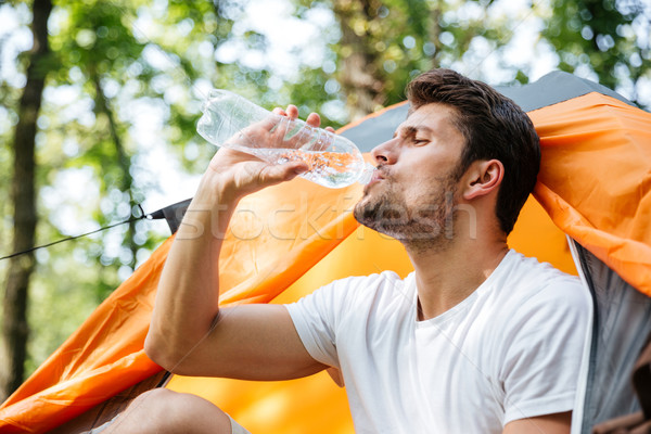 Attractive man tourist sitting and drinking water in touristic tent Stock photo © deandrobot
