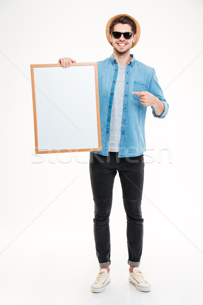 Happy young man holding blank whiteboard and pointing on it Stock photo © deandrobot