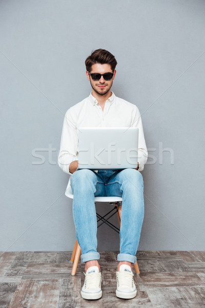 Feliz concentrado joven gafas de sol sesión usando la computadora portátil Foto stock © deandrobot